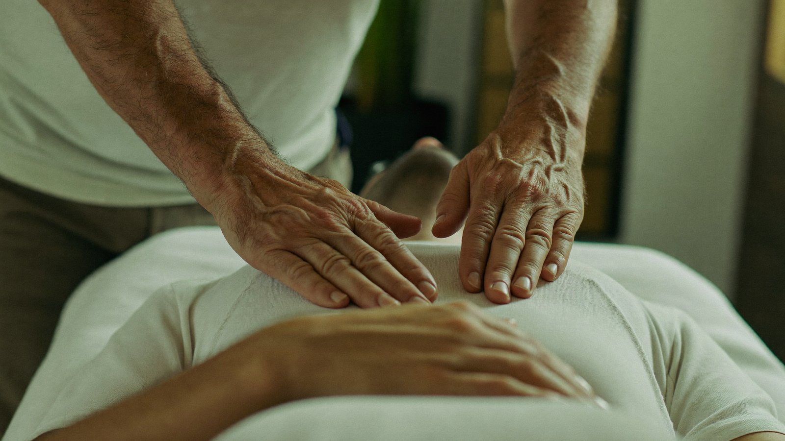 Reiki practitioner's hands resting lightly near a calm, clothed client before surgery
